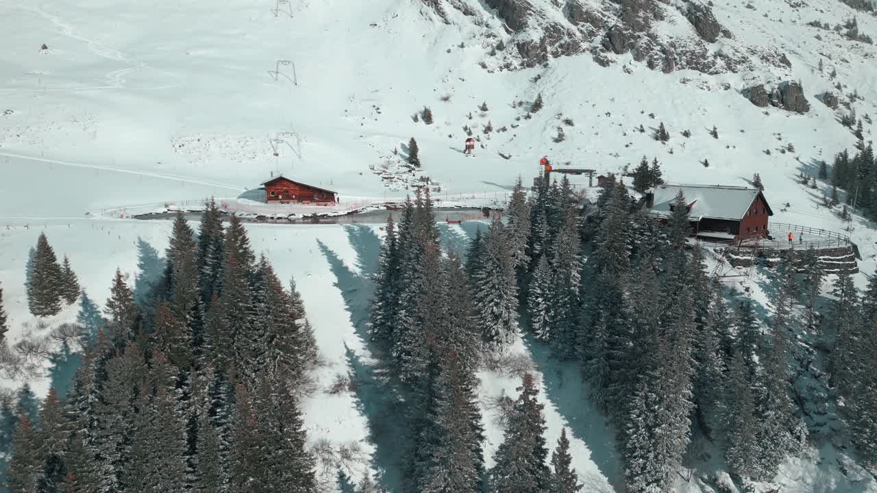 un dron se acerca a una cabaña junto a un lago artificial en una ladera nevada de los alpes y la parada del teleférico en engelberg, brunni, en bahnen, suiza