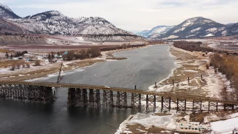 cars traveling across the wooden pritchard bridge over the south thompson river in winter surrounded by majestic mountains