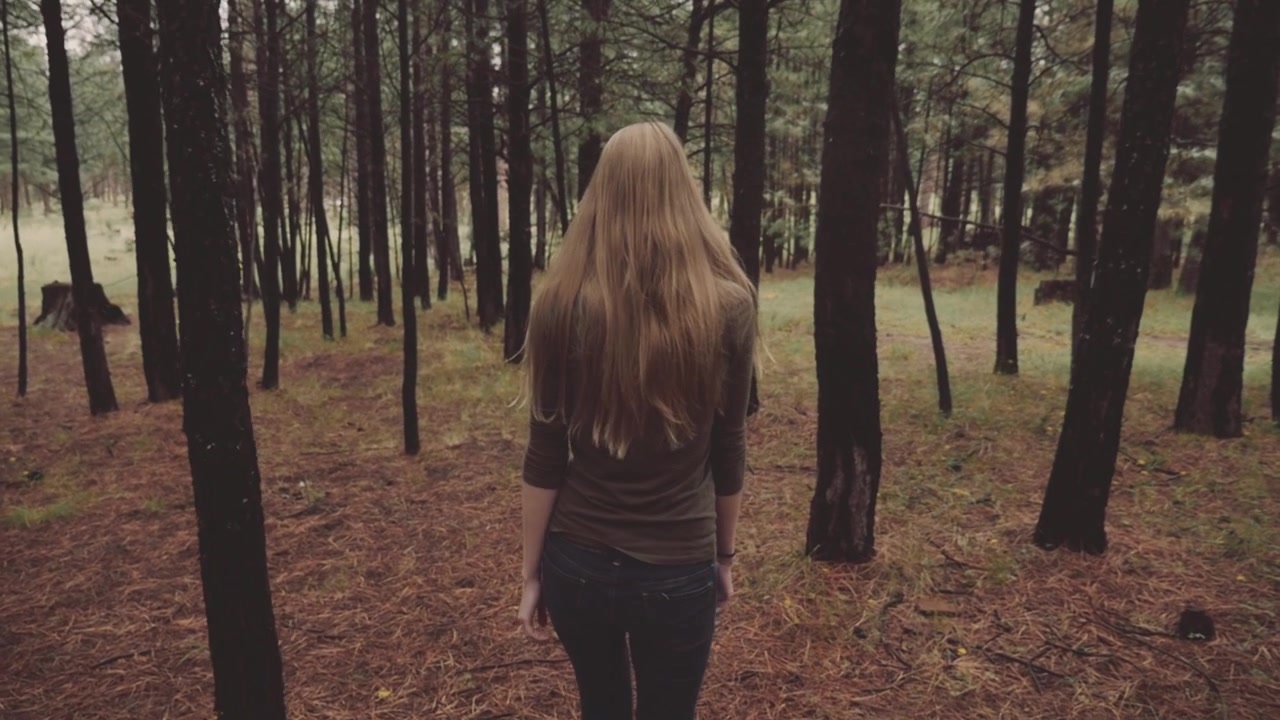 Jeune femme aux longs cheveux blonds marchant dans une forêt de pins
