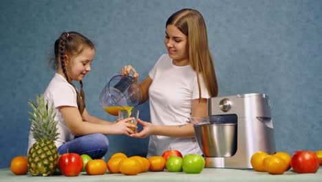mother and daughter in the kitchen. little girl drinks freshly squeezed juice. healthy drink. organic fruit and a modern squeezer on the table.