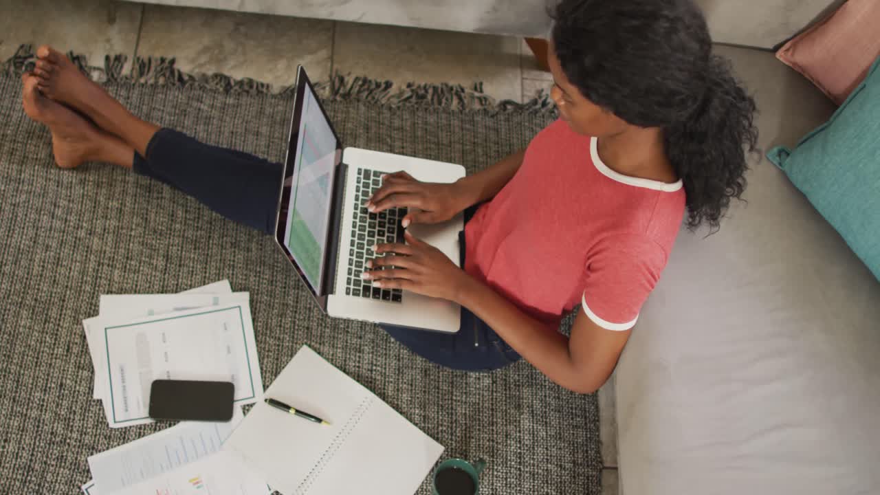 Video of happy african american woman sitting on floor using laptop