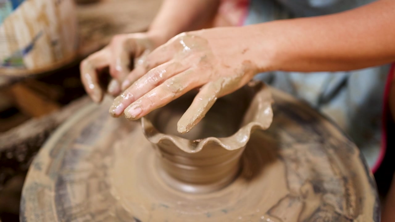 Primo piano delle mani di un vasaio che modellano un vaso di terracotta con bordi smerlati su un tornio.