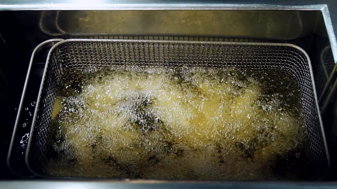 Processen med at friturestege pommes frites i olie. Flere stykker friturestegte kartofler placeres i friturekurven.