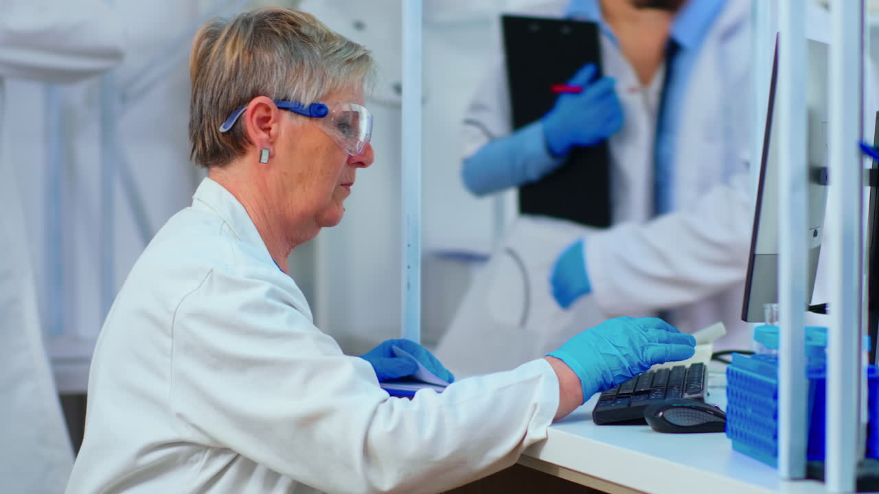 Senior biochemist typing and looking on pc analysing medical reports