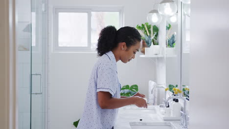 Woman-Wearing-Pyjamas-Standing-At-Sink-Brushing-Teeth-In-Bathroom