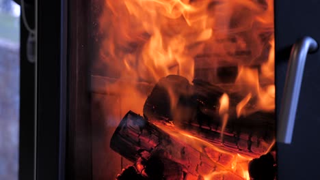 side shot of domestic home indoor fireplace with bed of red hot timber wood as orange flames fly upwards in slow motion