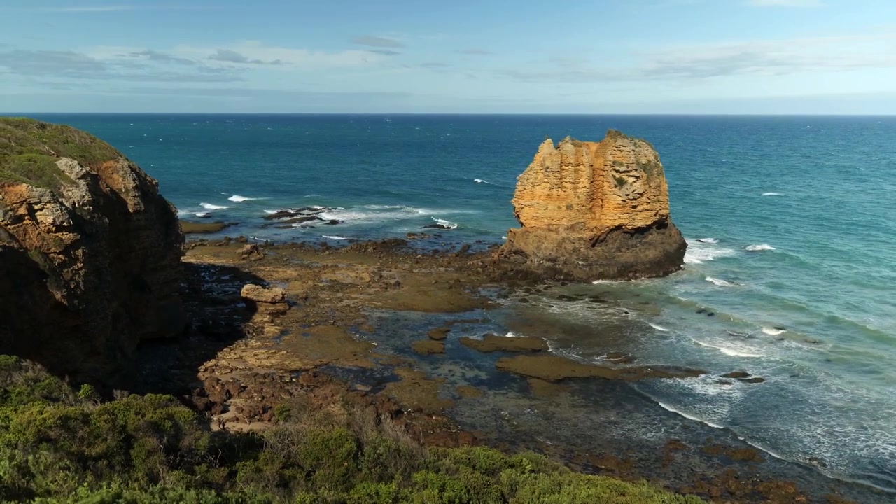 Una roccia isolata sulla costa, circondata da onde e scogliere frastagliate, che evidenzia la bellezza senza tempo dei paesaggi costieri