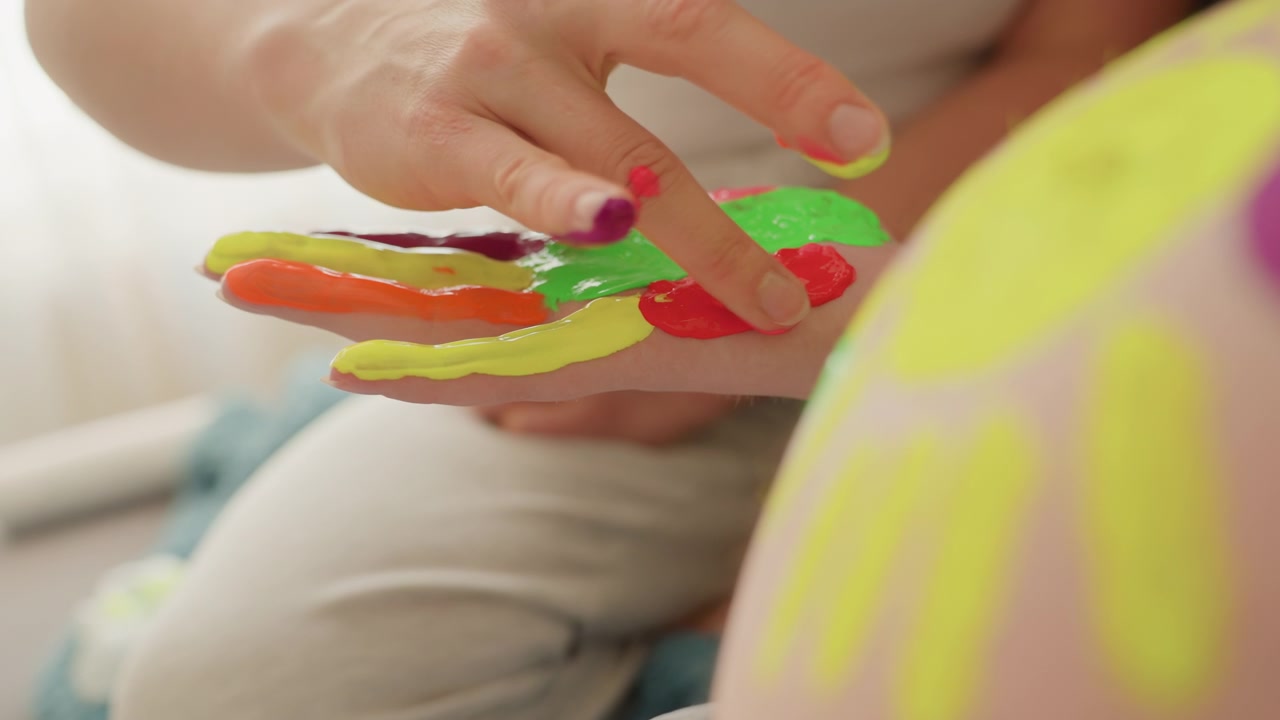 Detalhe da mão de uma mulher grávida pintando arte colorida na barriga