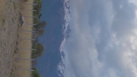 A-panoramic-of-snow-covered-mountains-with-wheat-fiels-and-trees-in-Patagonia,-Argentina