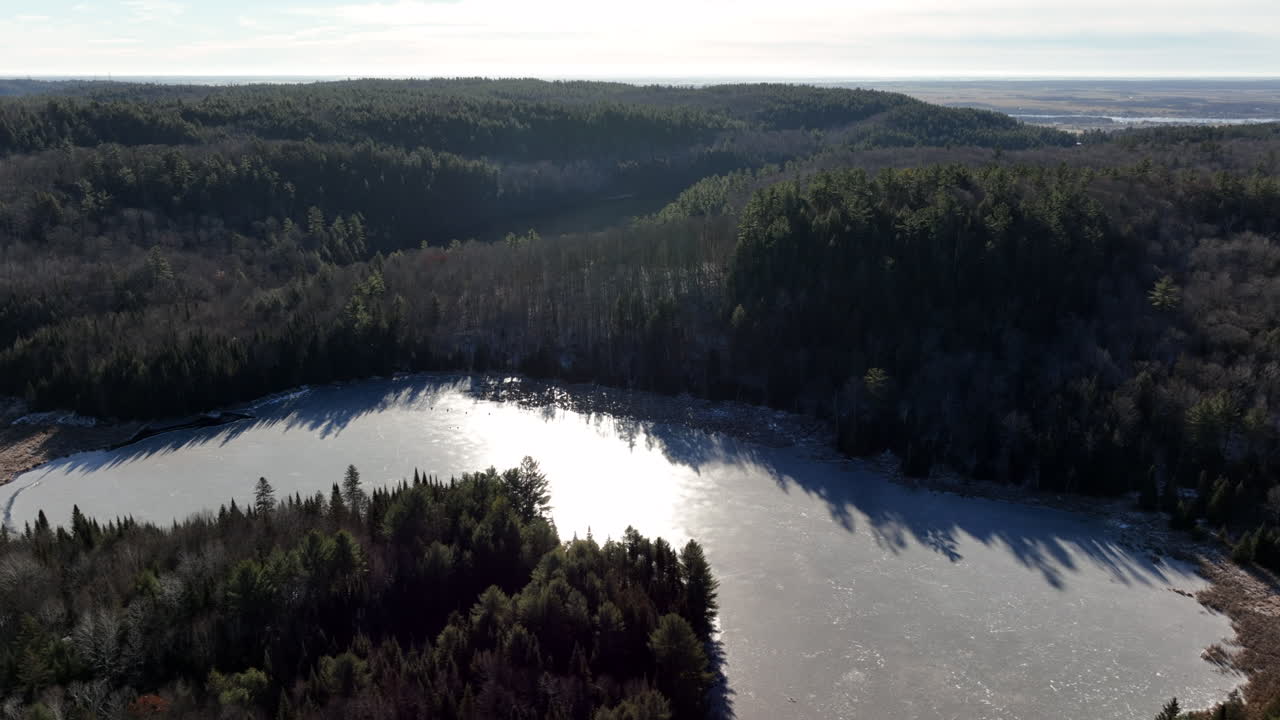 Frusen sjö med solreflektion vid soluppgången nära en lantlig skog under vintern