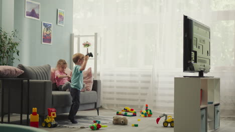 active little boy jumps while playing video game with sister