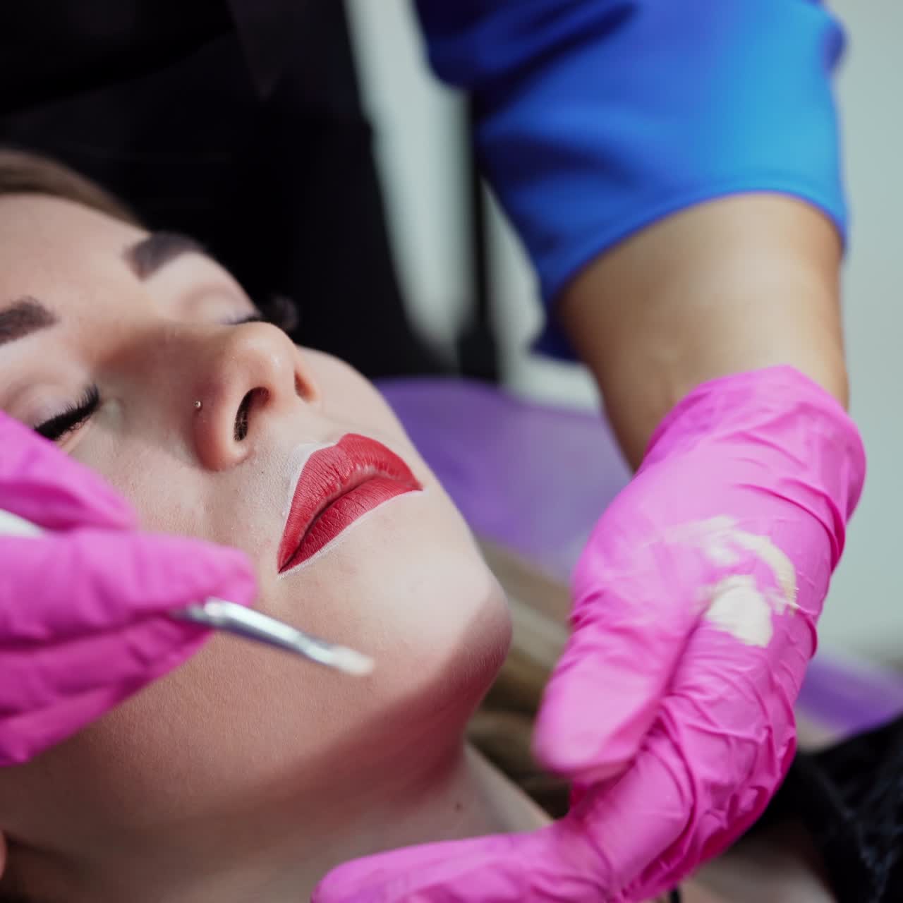 Beautician paints contour on woman's lips. Preparation before the permanent makeup on lips. Plastic medicine and cosmetology.
