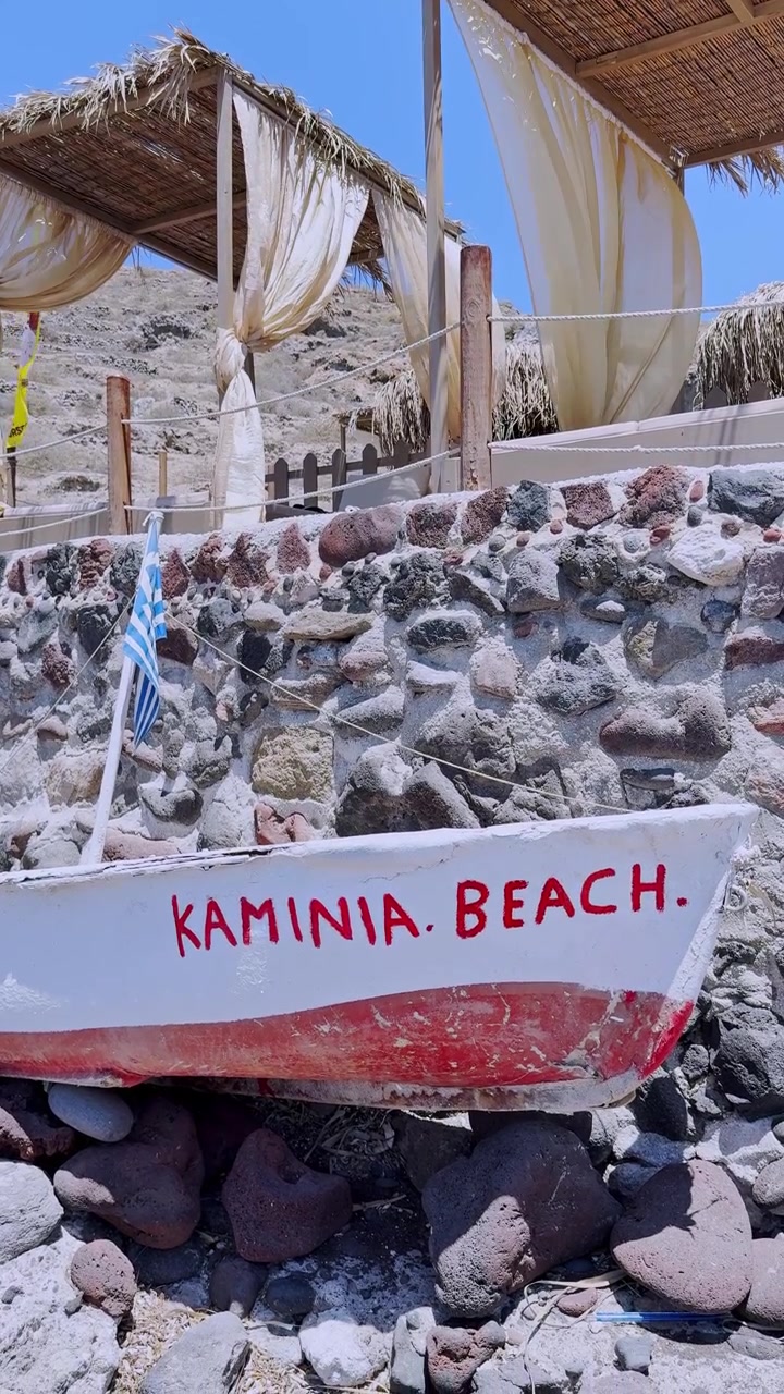 Santorini'deki Kaminia Plajı'nda Yunan bayraklı beyaz tekne.
