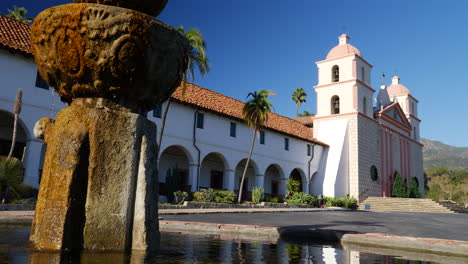 the historic santa barbara mission building with spanish catholic architecture and fountain reflecting and splashing water slide right