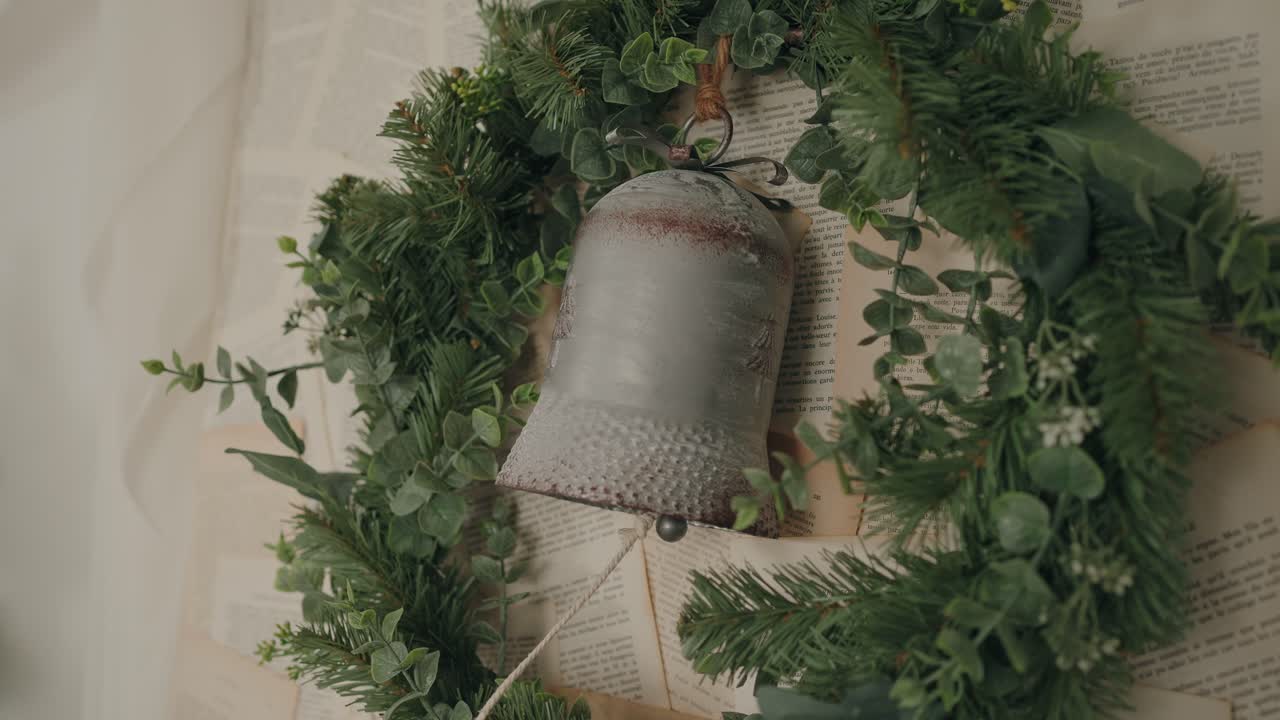 Festive wreath with bell ornament, evergreen leaves, and vintage book pages in the background - slowmo
