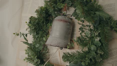festive wreath with bell ornament, evergreen leaves, and vintage book pages in the background - slowmo