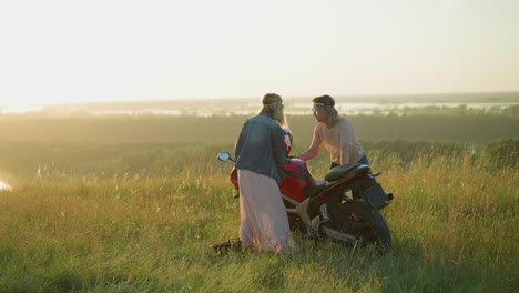 two sisters are joyfully cleaning a motorcycle and dancing in an open grassy field at sunset
