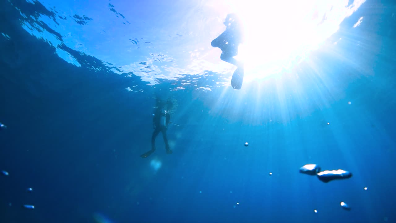 Scuba divers float on ocean surface with sun rays, low angle