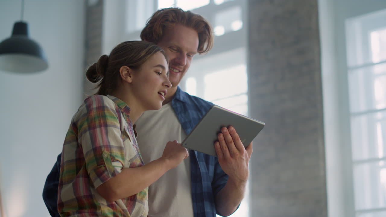 Cheerful couple enjoying design of house renovation with tablet indoors.