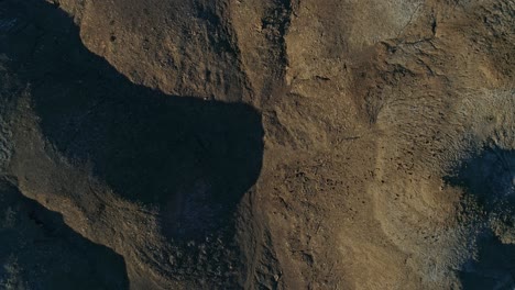 Slow,-aerial-downward-view-moving-over-dry,-barren-mudstone-embankments-in-a-desert