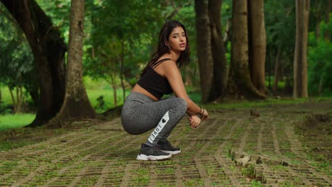 In-the-midst-of-a-tropical-park,-a-young-girl-works-out,-adorned-in-sports-wear-doing-squats