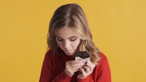 una adolescente caucásica comiendo una barra de chocolate y sonriendo.