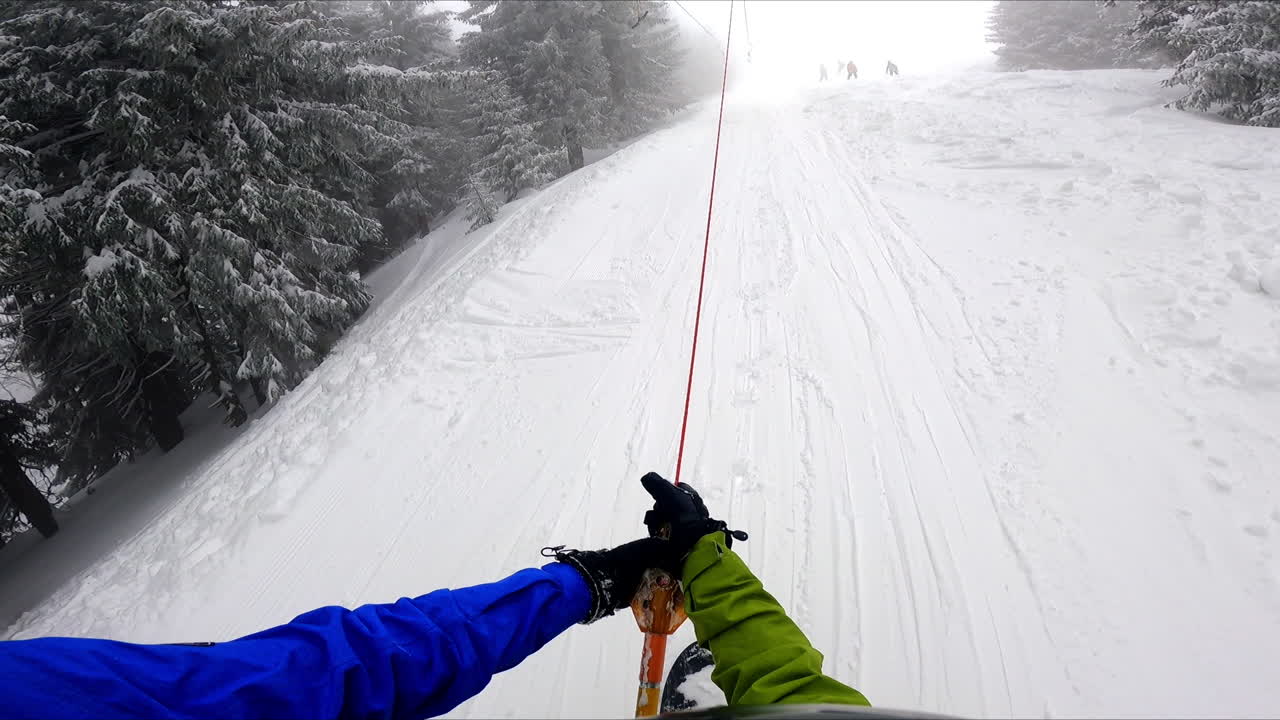 Sportsman hold by the funicular moving up the slope. Group of snowboarders stand in the snow.