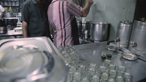 man preparing traditional filter coffee in a busy kitchen in bangalore, karnataka india
