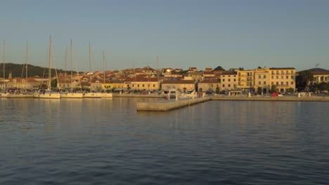 Das-Licht-Des-Sonnenuntergangs-Trifft-Auf-Den-Betonpier-Mit-Segelbooten-Und-Die-Gebäude-Entlang-Der-Küste-Von-Vela-Luka-In-Kroatien