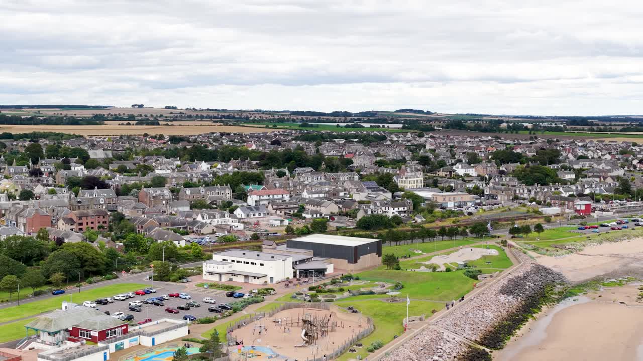 Drone glides over Dundee, Scotland, revealing town, parks, coastline, and overcast sky