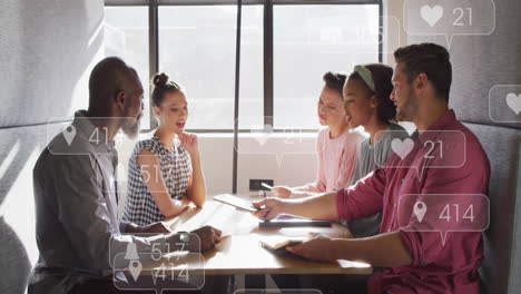 Diverse team discusses under floating social media icon, symbolizing tech integration.