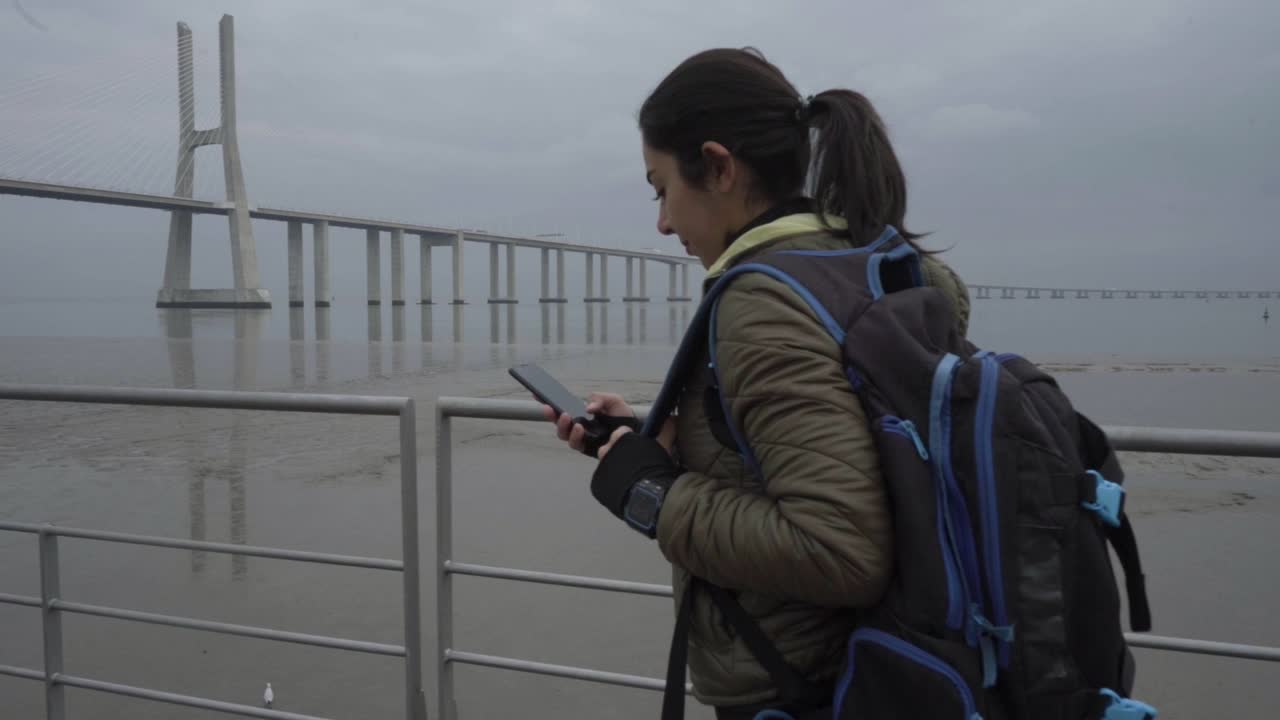 vista lateral de una mujer joven sonriente usando un teléfono inteligente