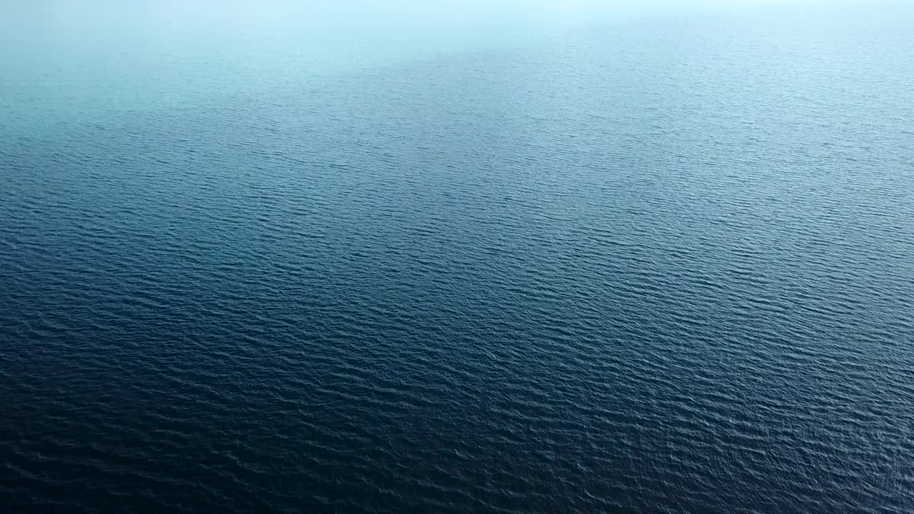 Aerial rising view of dark blue and turquoise water