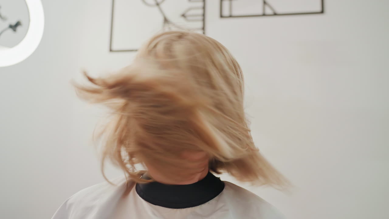 Donna caucasica bionda che si scompiglia i capelli, ring light da studio e mantello bianco incorniciano un caschetto biondo all'altezza delle spalle mentre ruota, ciocche che volano con sfocatura dinamica, energia giocosa e lucentezza raffinata, modello