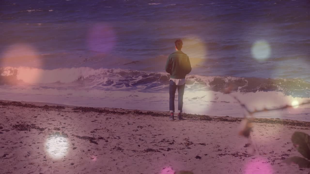 Mand står ved kystlinjen, kigger ud over havet, med flydende pastel bokeh sundhedsikoner