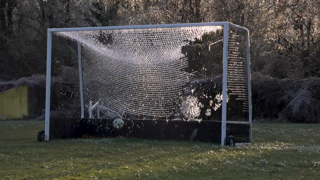 SLOW MOTION: A soccer ball slams an icy net of a soccer goal exploding shattered ice into the air