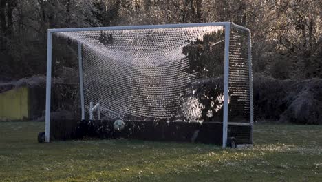 slow motion: a soccer ball slams an icy net of a soccer goal exploding shattered ice into the air