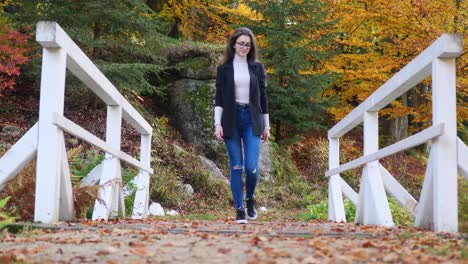 teenage girl in a casual clothes walking over bridge in colorful park on autumn day, slow motion