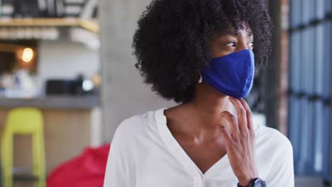 african american woman wearing face mask sitting in cafe looking at window