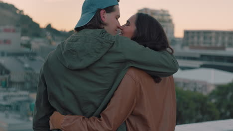 young caucasian couple kissing on rooftop embracing romance sharing intimate connection hanging out enjoying view of city at sunset