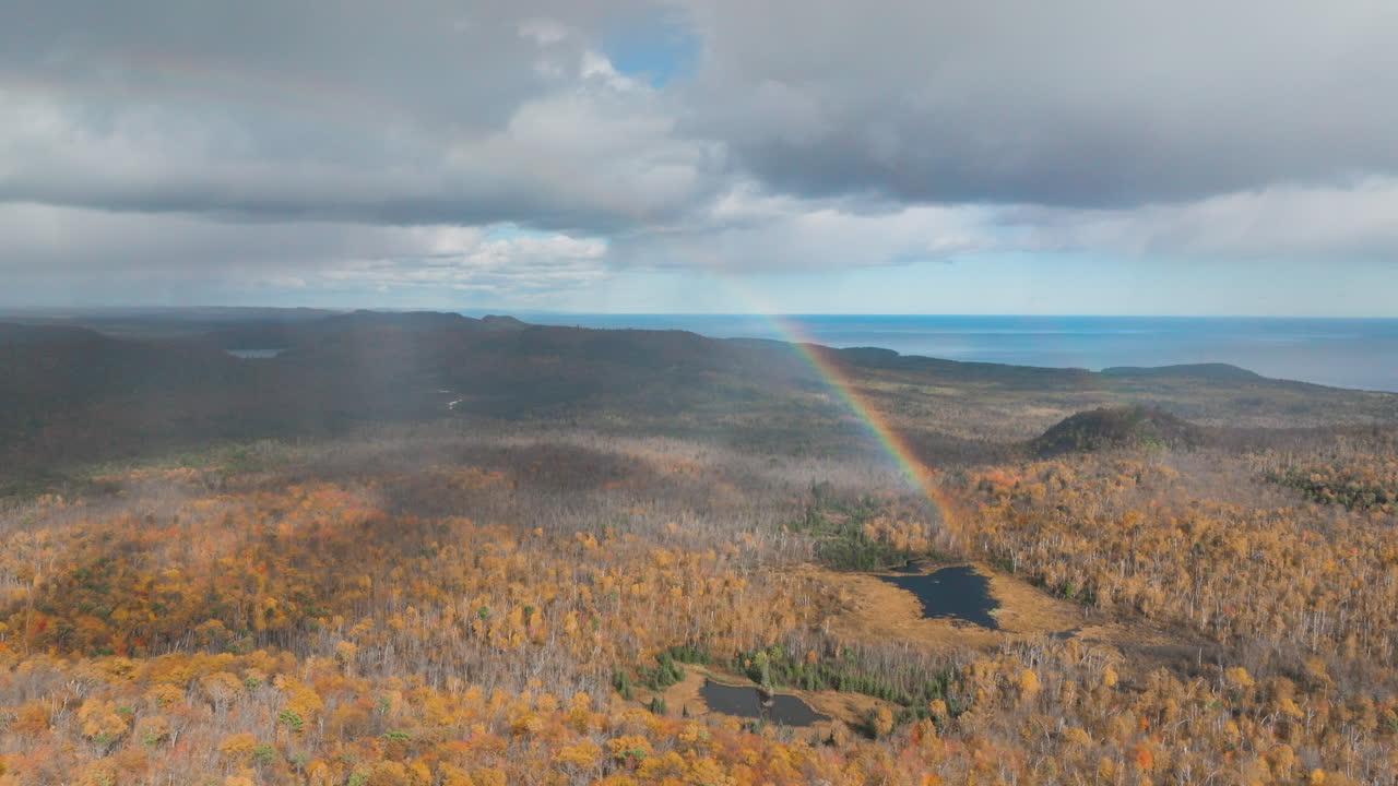 vista aérea de un arco iris y lluvia sobre el bosque de otoño con el lago superior en la distancia