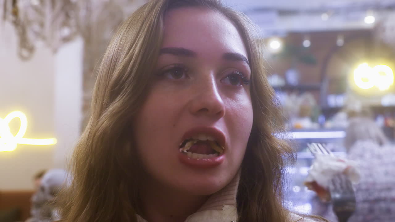 Close-up of young woman eating creamy croissant with fork in cozy cafe, enjoying dessert. Whipped cream and fruit topping visible, highlighting the indulgent, relaxed atmosphere