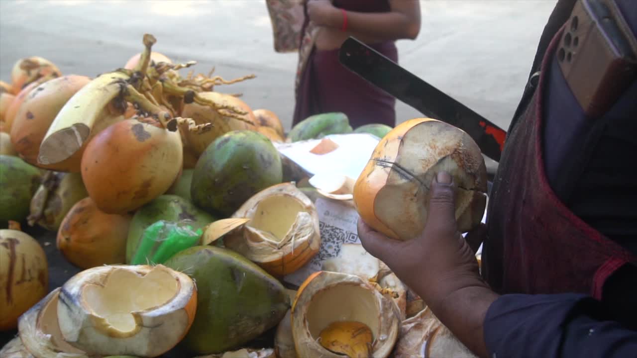 The coconut water seller is giving the coconut’s malai (pulp) to a lady while cutting the coconut.USP