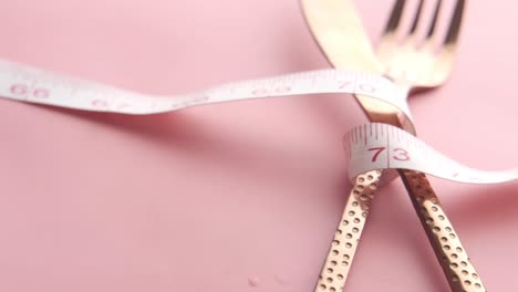 measuring tape wrapped around cutlery on pink background