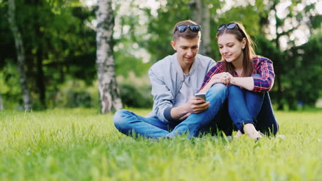 a man and a woman enjoying a mobile phone they sit side by side on the grass in the park hd video