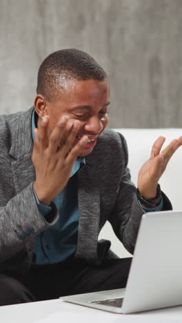positive african-american man tells funny story to colleagues at online meeting via modern laptop computer sitting at table in living room slow motion