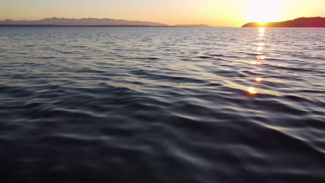 Drone-flying-low-over-the-waves-along-the-Puget-Sound-at-sunset,-Washington-State