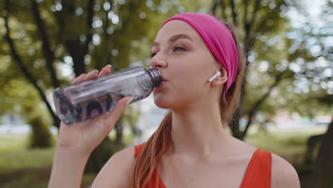 Athletic-fit-sport-jogger-young-woman-drinking-water-from-bottle-after-training-exercising-in-park