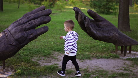 little boy touches the wooden sculpture of big hands. child walking in the green park in summer.