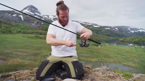 Hombre-Cocinando-Comida-Al-Aire-Libre-Mientras-Fija-La-Línea-De-Una-Caña-De-Pescar-En-El-Parque-Nacional-Lomsdal-visten,-Nordland,-Noruega